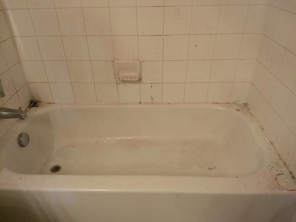 Bathtub with stained caulk and dull surface before cleaning