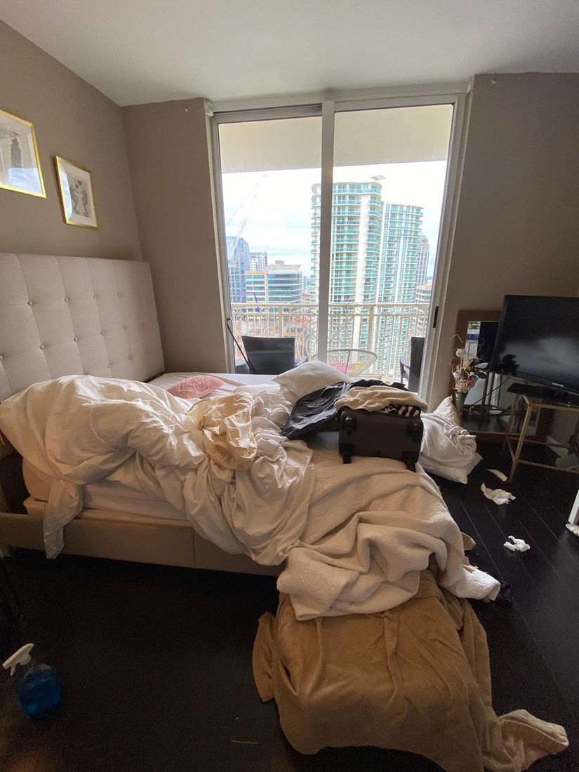Messy bedroom with clothes and bedding piled on the bed before cleaning