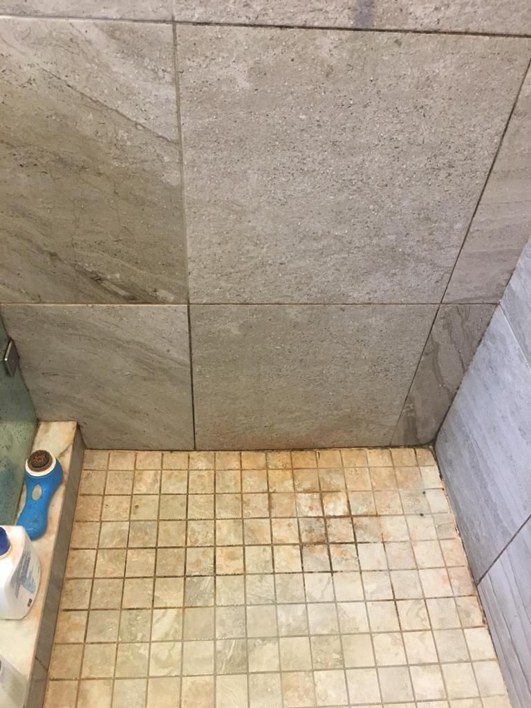 Shower floor tiles with rust-colored stained grout before cleaning